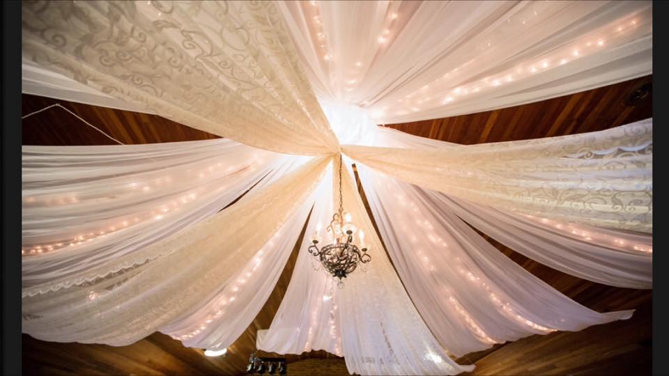 White linens draped from the ceiling surrounding a gorgeous light fixture, all party rentals from Devine Wedding Design.