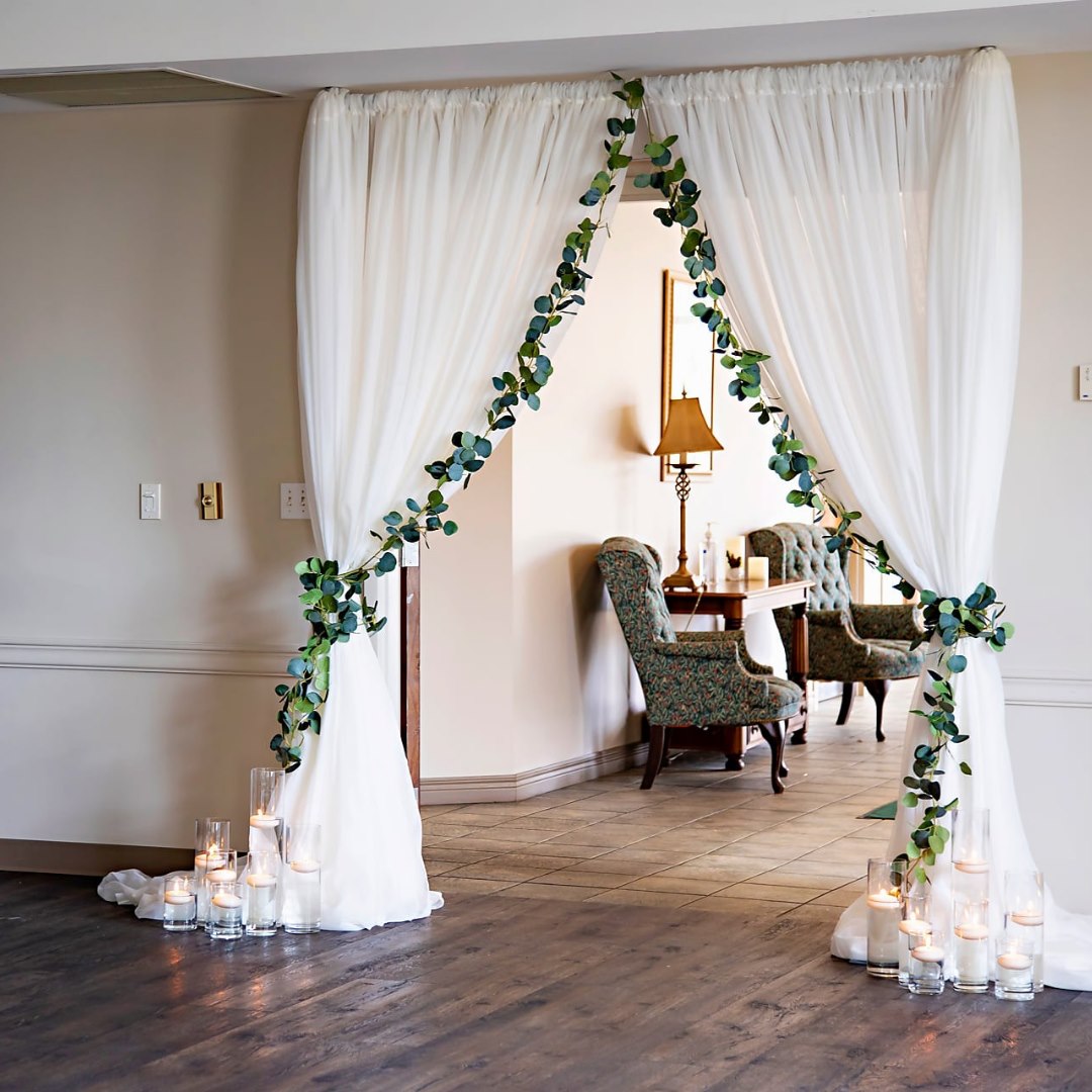 A wide entry way decorated with white linens, greenery, and candles from the wedding rentals gallery.
